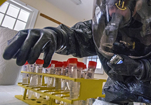 Man in a protective suit and helmet picks through vials with a gloved hand