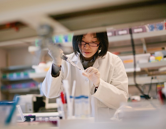 Asian woman with glasses in a lab coat with a syringe