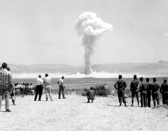 Mushroom cloud in the distance with onlookers in the desert, day time