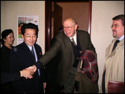 Lewis in the center smiling with outstretched hand with Ri Hak Gwan and Pritchard at his sides