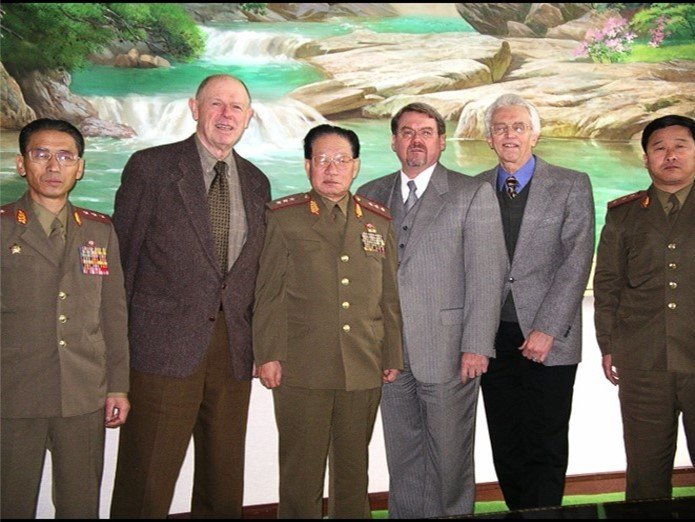 Group of North Korean military officers with 3 Americans in front of a big painting