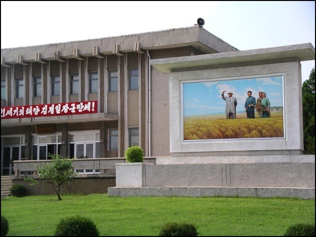 Administrative building with a mosaic of men standing in a field and a green lawn in front