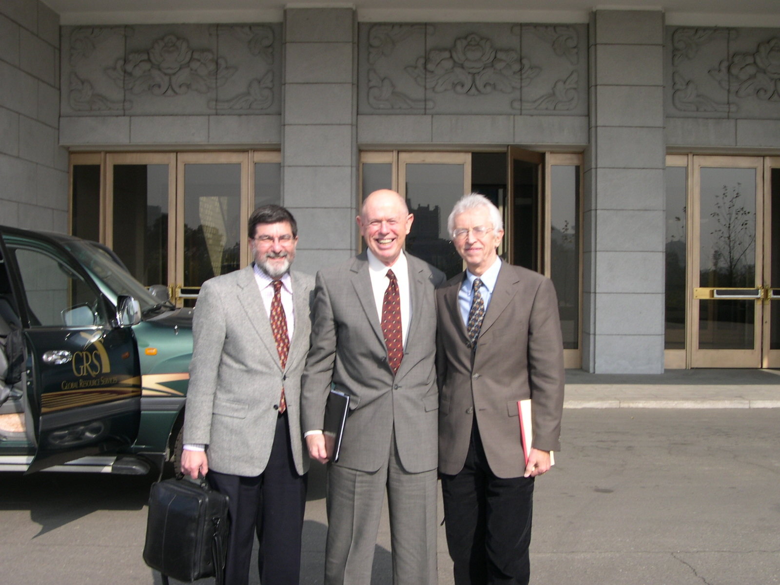 Three men in business suits standing outside a building and smiling at the camera