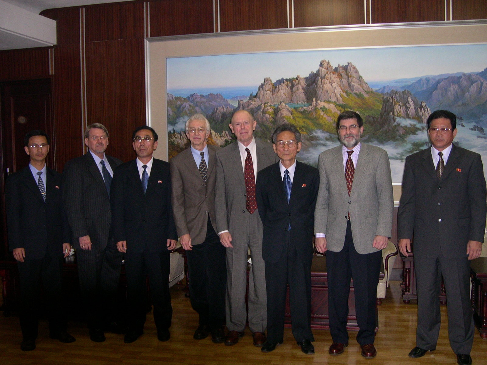 Large group of men in business suits posing in front of a wall-sized landscape painting
