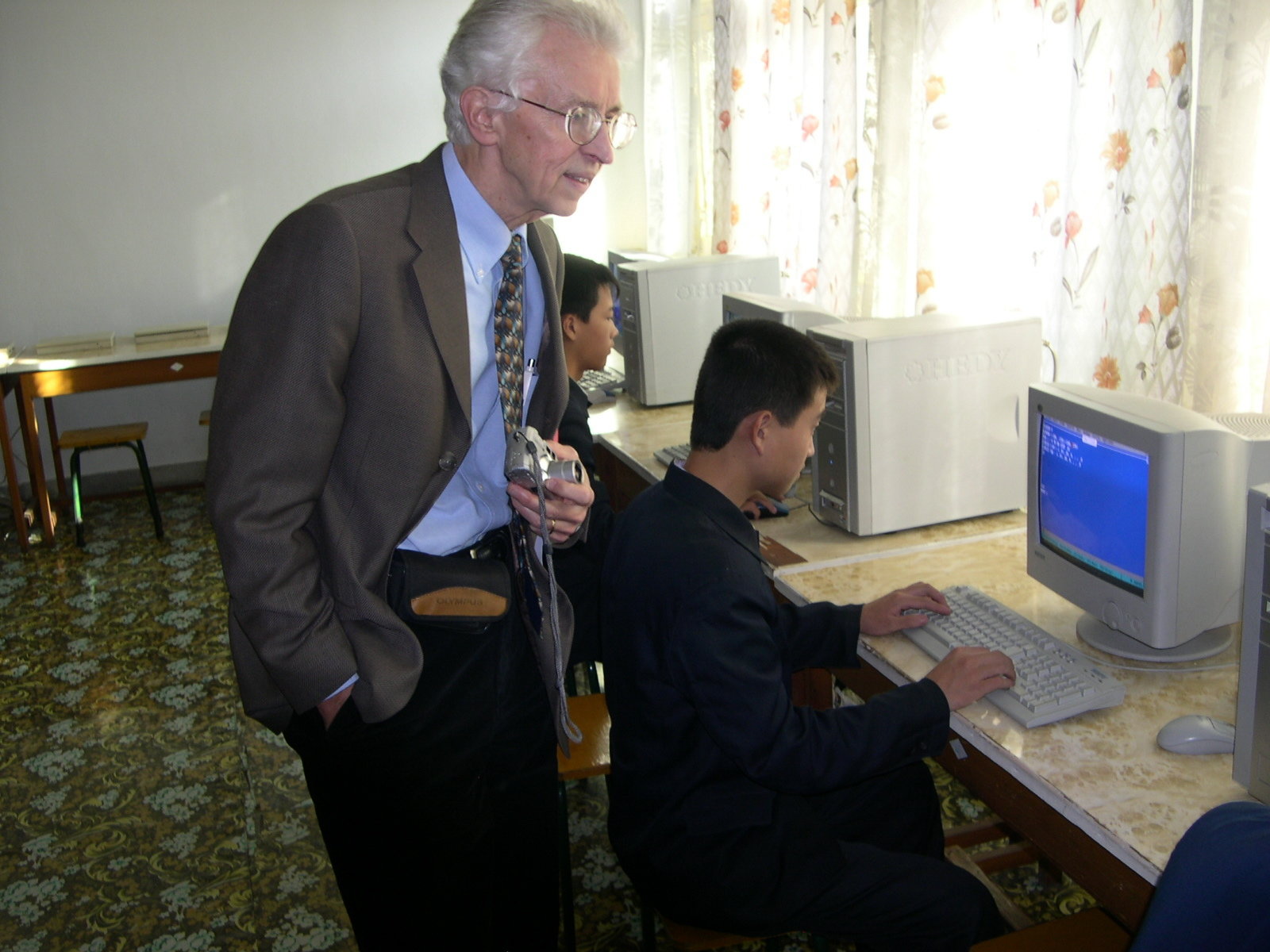 Man looking with interest at the screen of a desktop computer with students sitting in front of their monitors