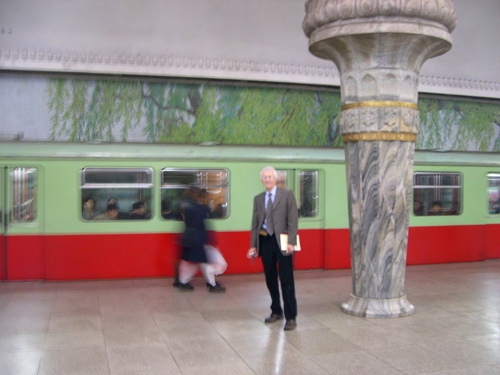 Man standing on a marble-paved platform in front of a green and red subway car