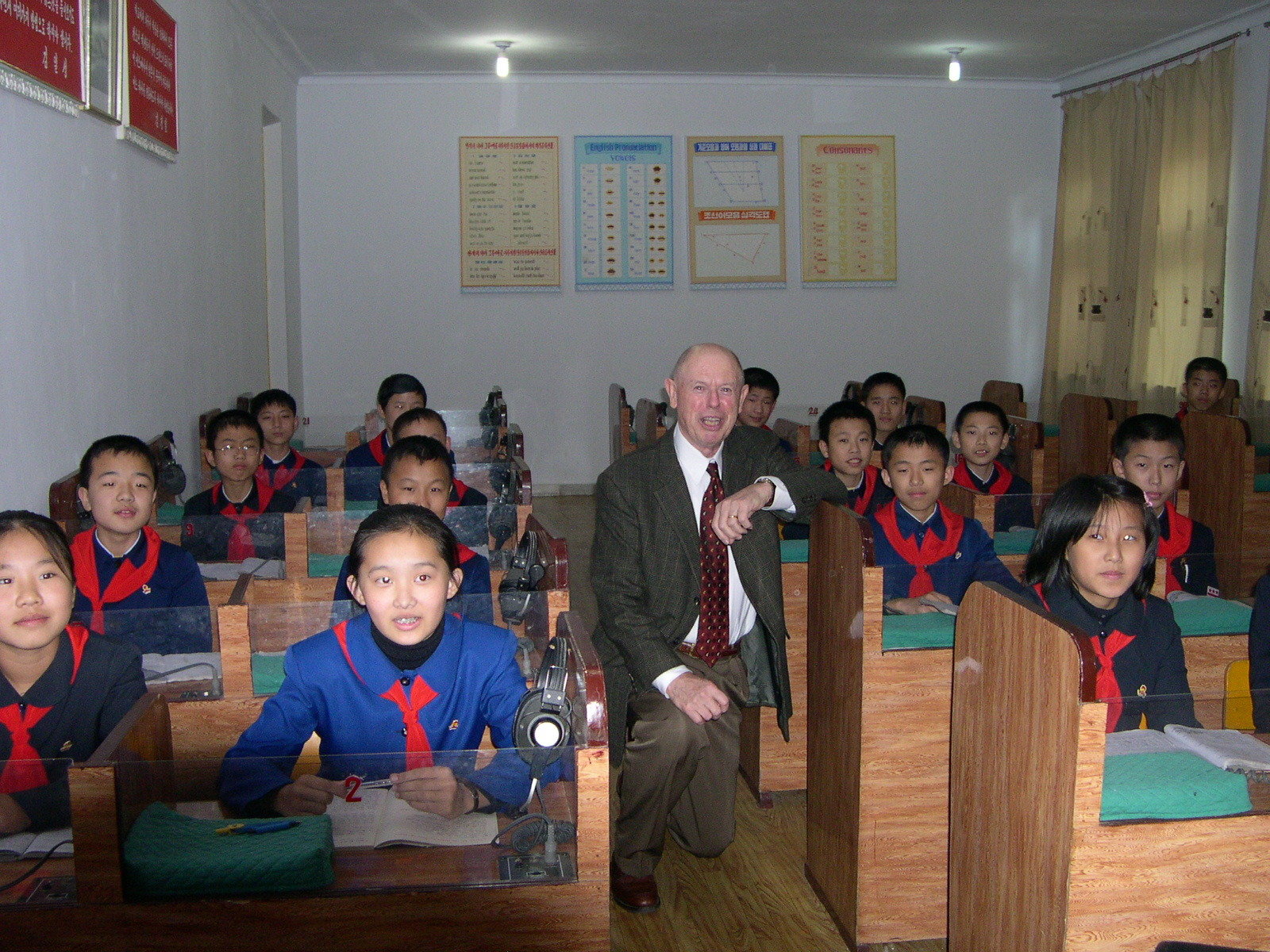 Man kneeling next to school desks with students sitting in pairs