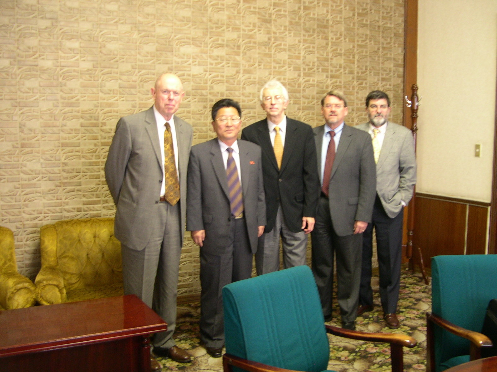 Five men in business suits pose for a photo inside a hotel conference room