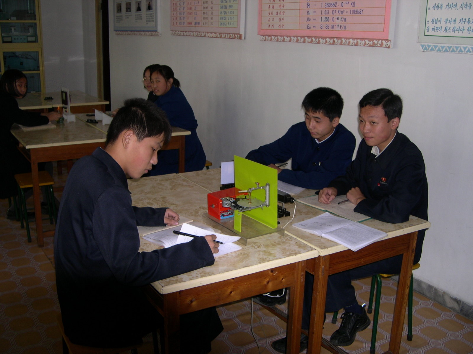 Three uniformed students at a desk busy with a physics tabletop installation.