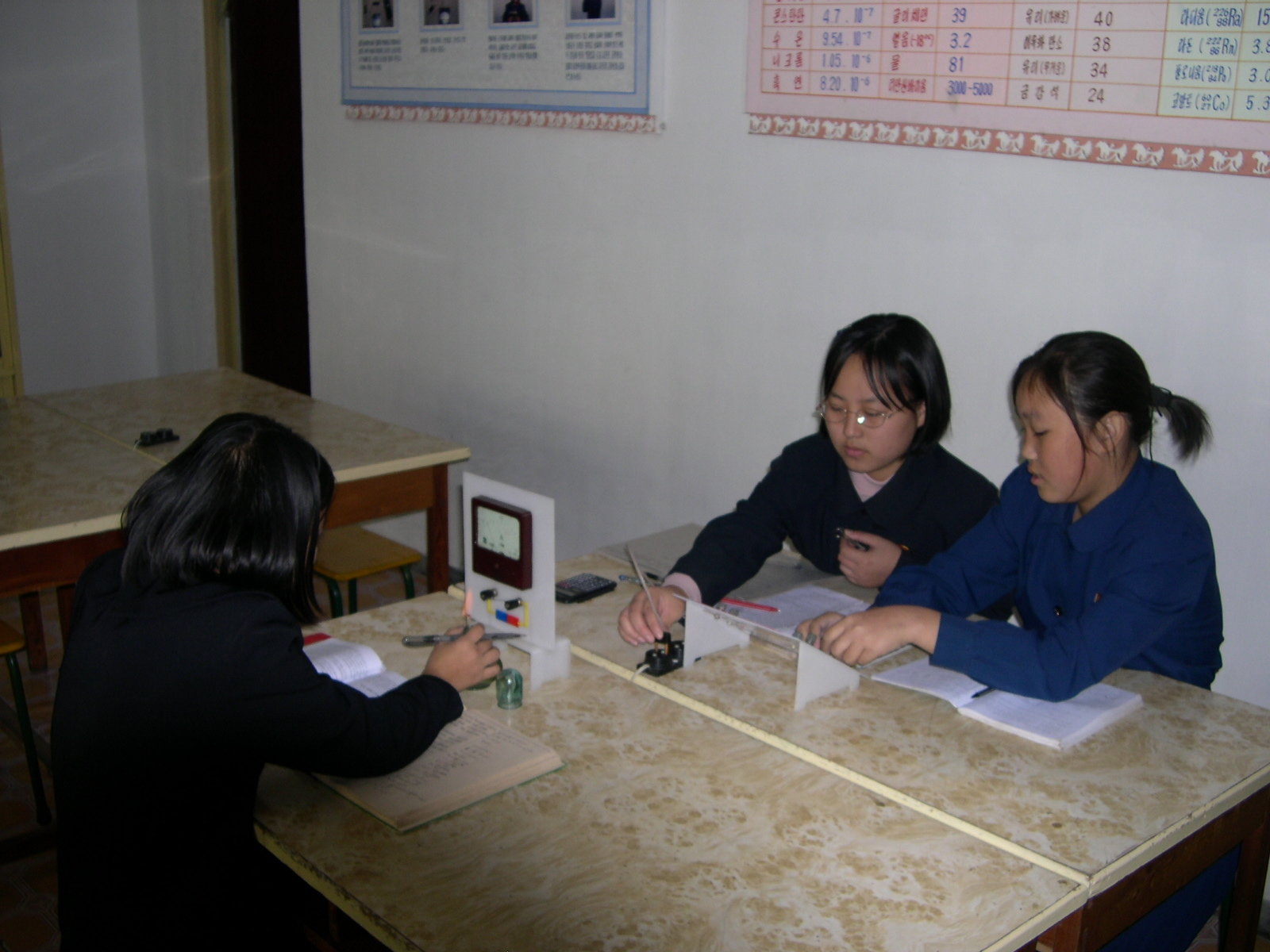 Three girls in student uniform are conducting physics tabletop experiment