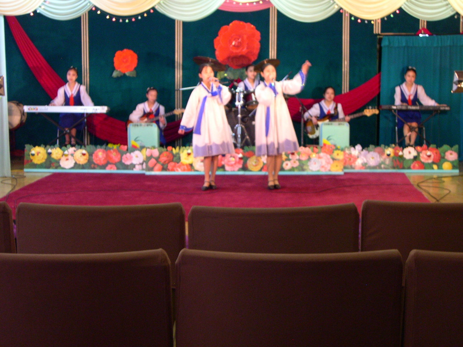 Two girls in folk dress perform a dance on a decorated scene