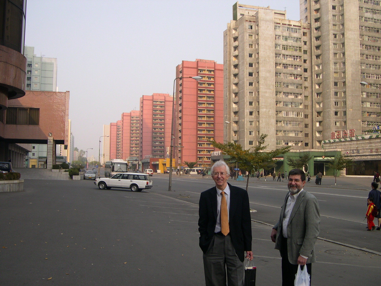 Two men with purchase bags standing on a broad side walk lined with high rise residential buildings
