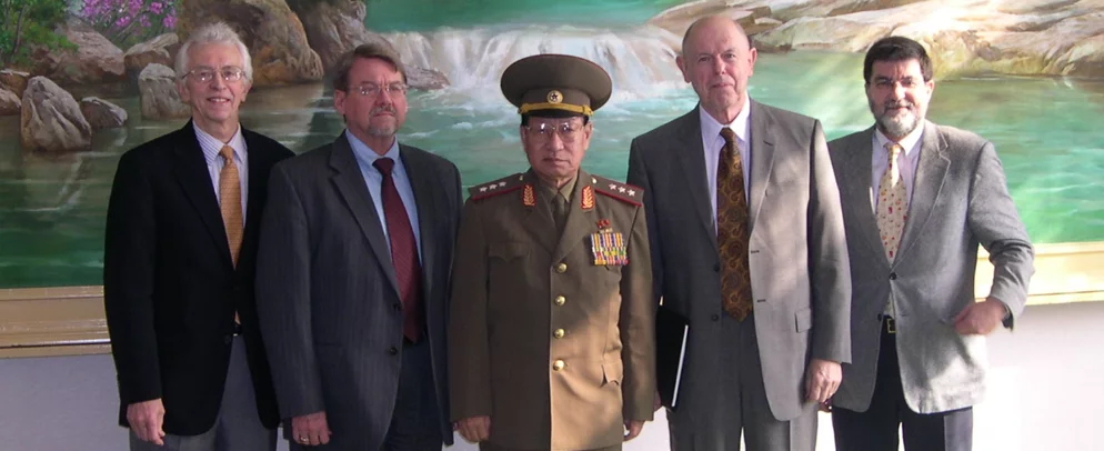 Four members of the Stanford delegation with a high ranking North Korean Officer and a painting in the background