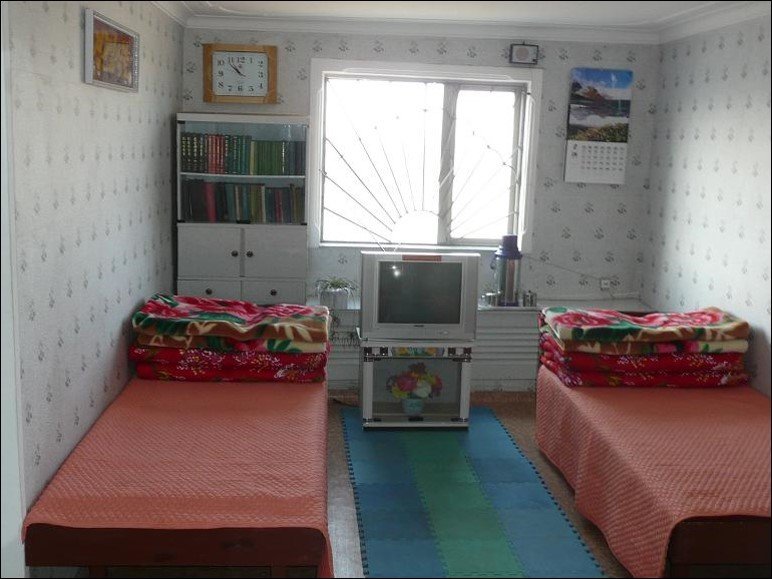 Two neatly made single beds with a TV set between them and a bookshelf with many books