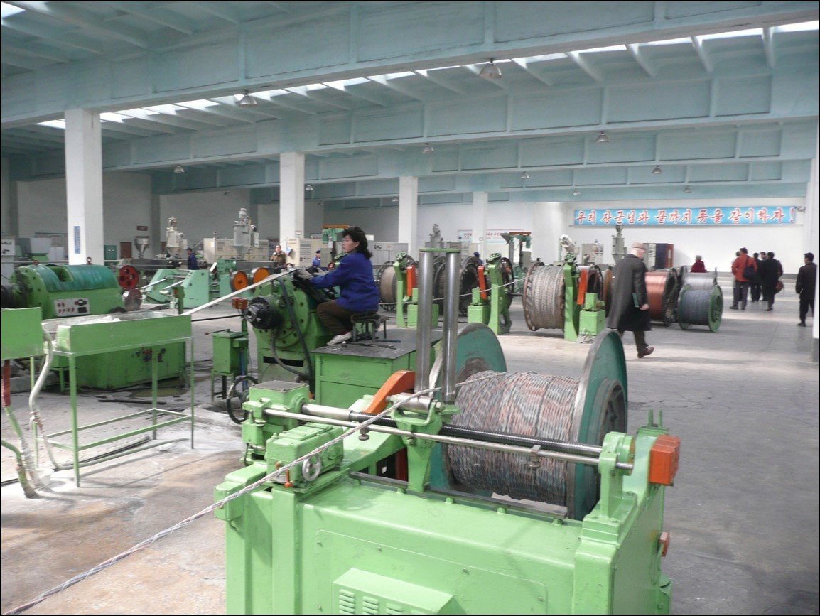 Machines in a large factory space and a woman operating another machine