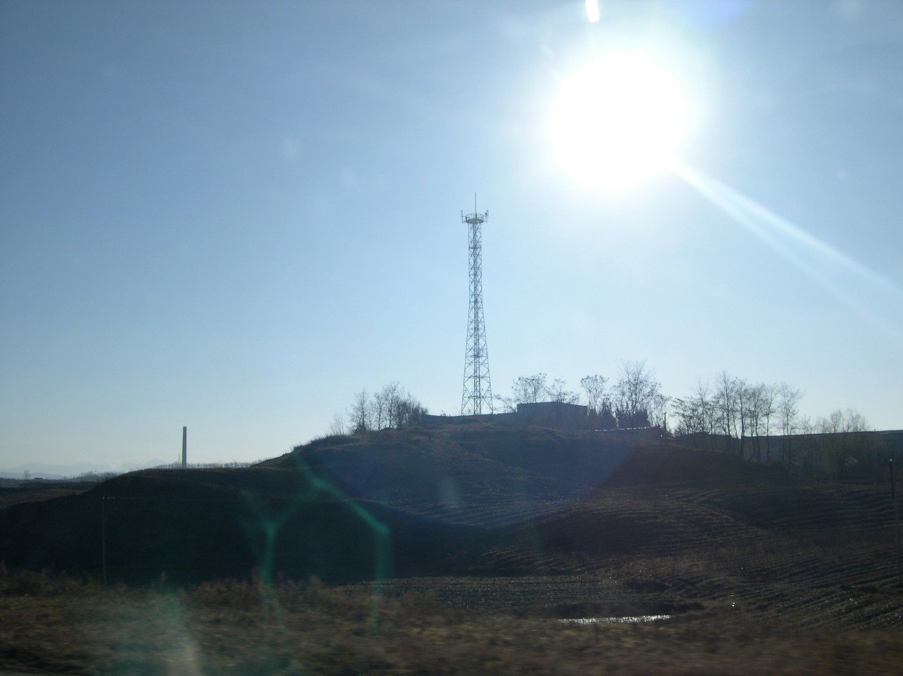 Cell towers on a hill with the sun and a lens flare