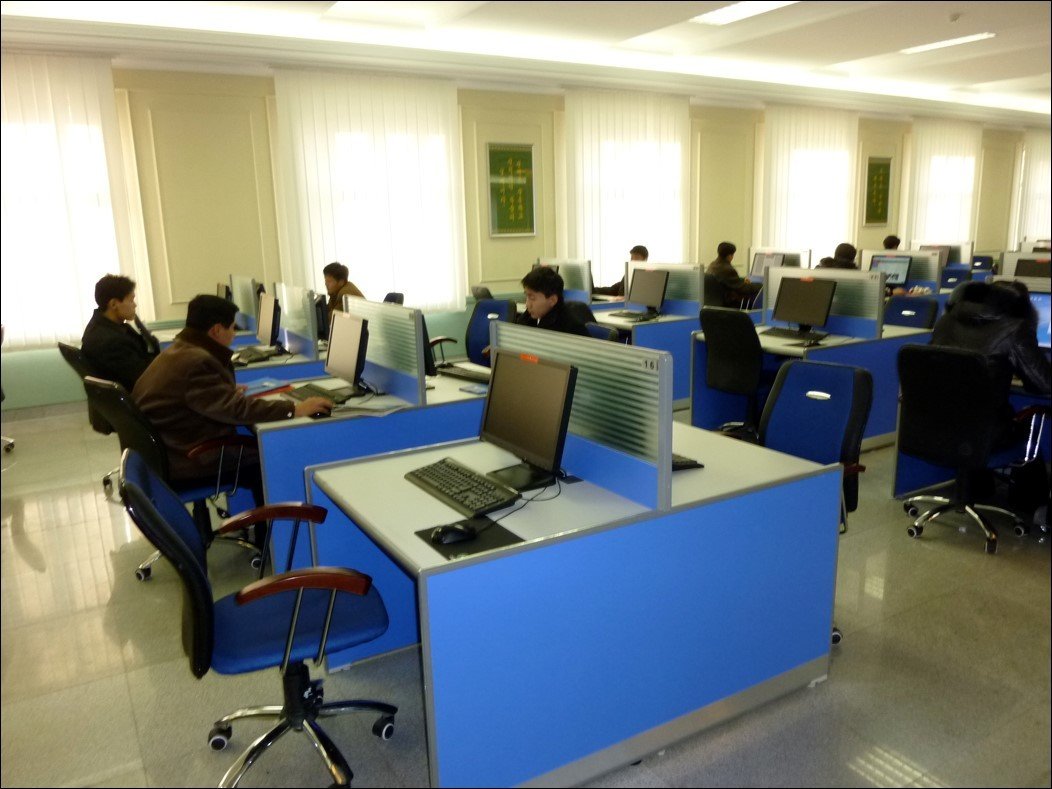 Large room with blue desks partitioned in the middle with desktop stations. Students sitting at some desks looking into monitors.