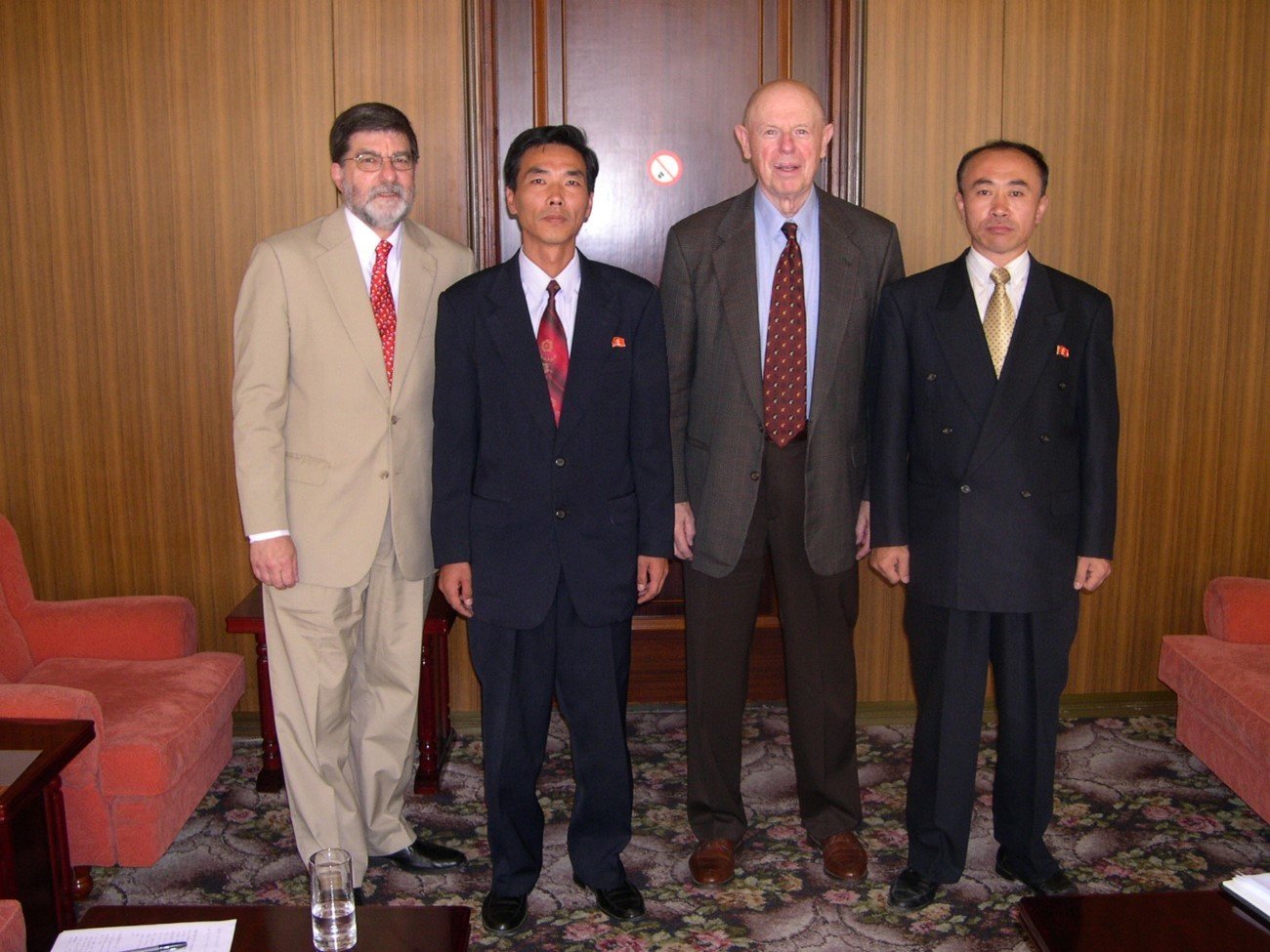 Two Americans and two Koreans in suits and tie posing for a photo in a carpeted room with soft furniture