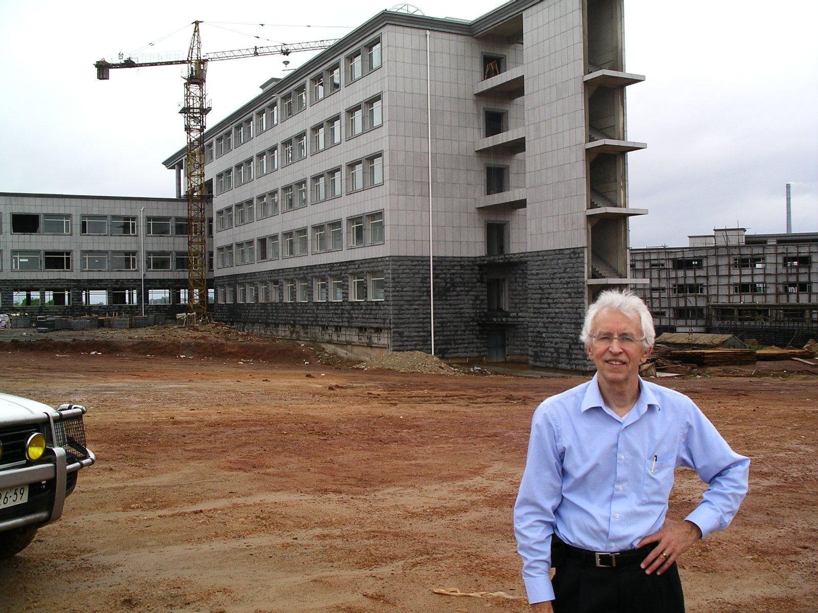 Hecker in blue shirt posing at an empty construction site with a building being constructed at the background