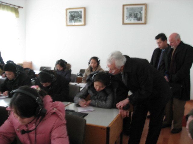 Man leaning down to the student desk to see into the notebook of a student