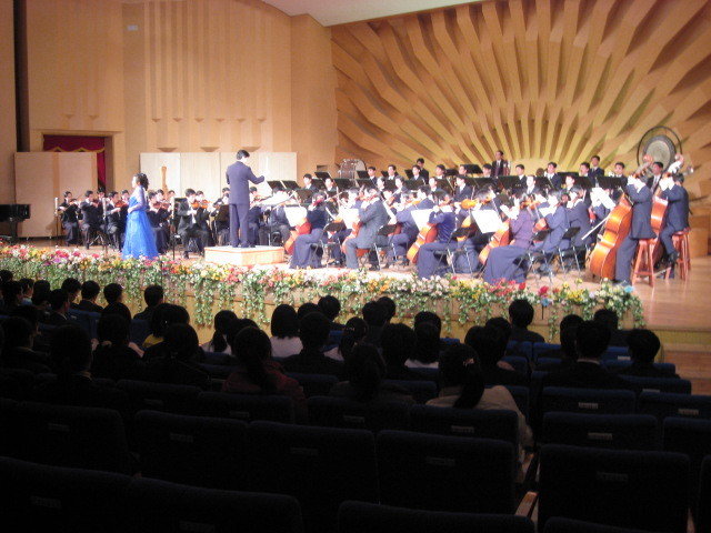 View of scene with a woman in blue concert dress singing to the orchestra