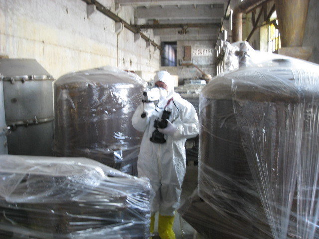 Man in protective suit video recording among tanks wrapped in plastic