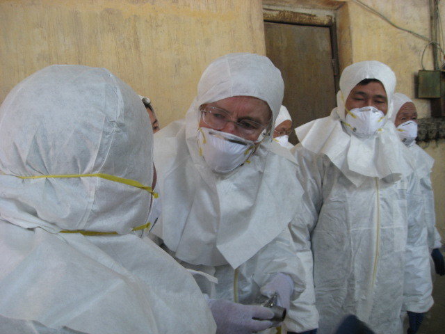 Man in white protective suit and respirator leaning to another man shown from the back in conversation