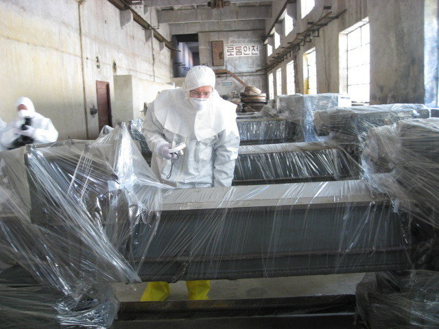 Man in protective suit leaning over a massive lathe wrapped in plastic