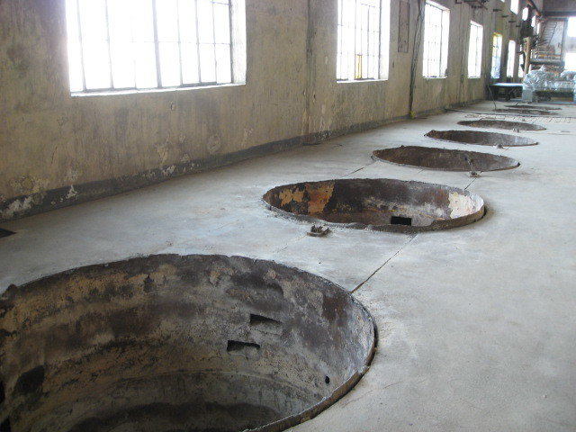 A row of empty pits in the concrete floor with light streaming from large windows