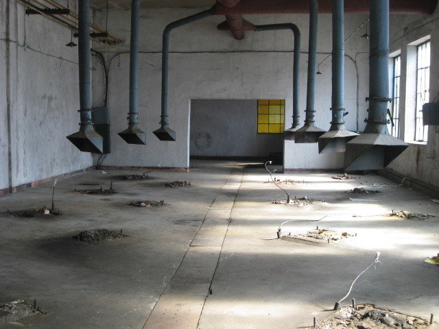 Empty space with seven metal hoods hanging down from the high ceiling on long connector pipes