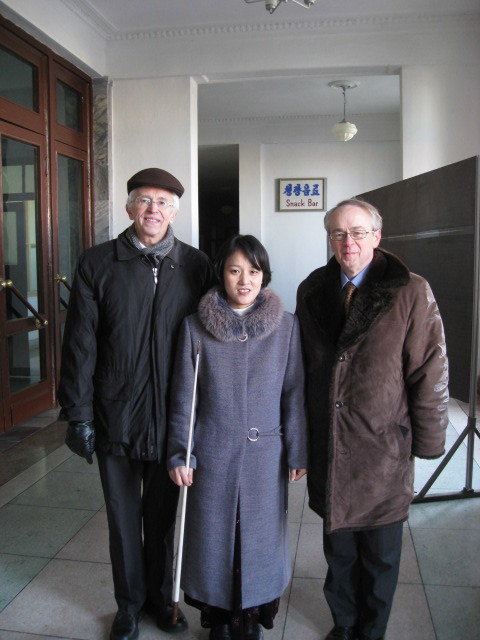 Two men in winter coats posing for photo with a young Korean female museum guide at the exit of a museum