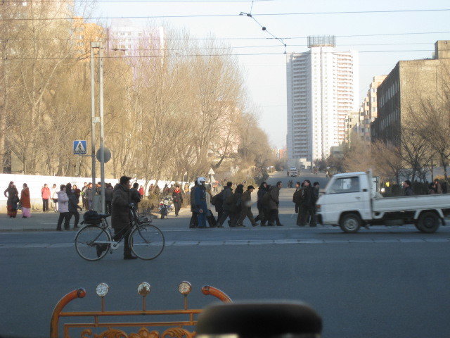 Sidewalks are very busy on a cold Pyongyang morning. Lots of people moving in groups, two women in traditional long robes under winter jackets