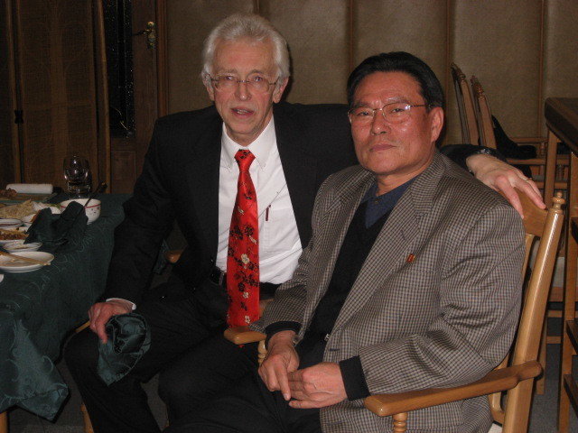 An American (Hecker) in red tie and a Korean seated next to each other and turning to pose for photo