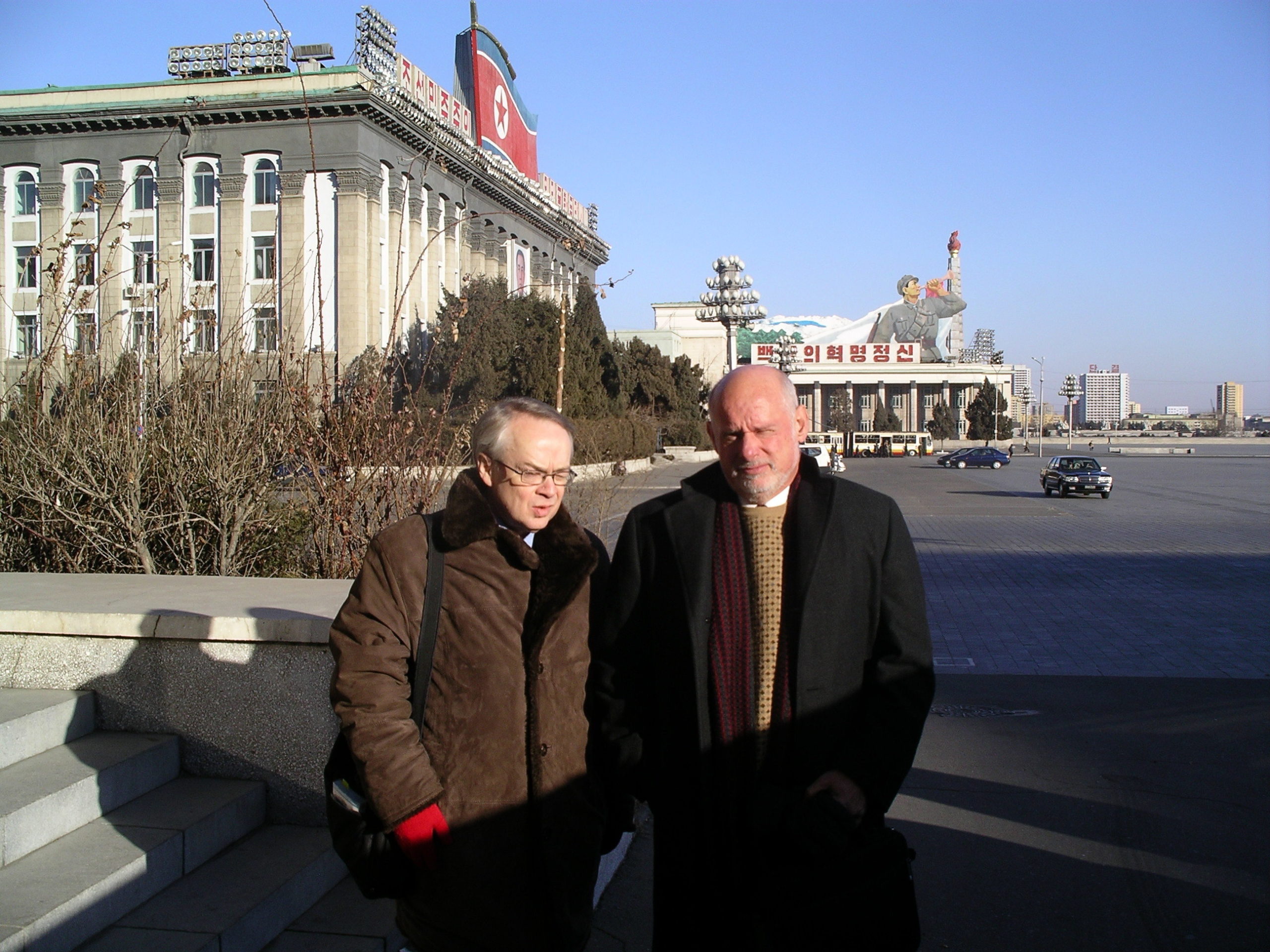 Two men posing for photo with the Pyongyang main square at the background