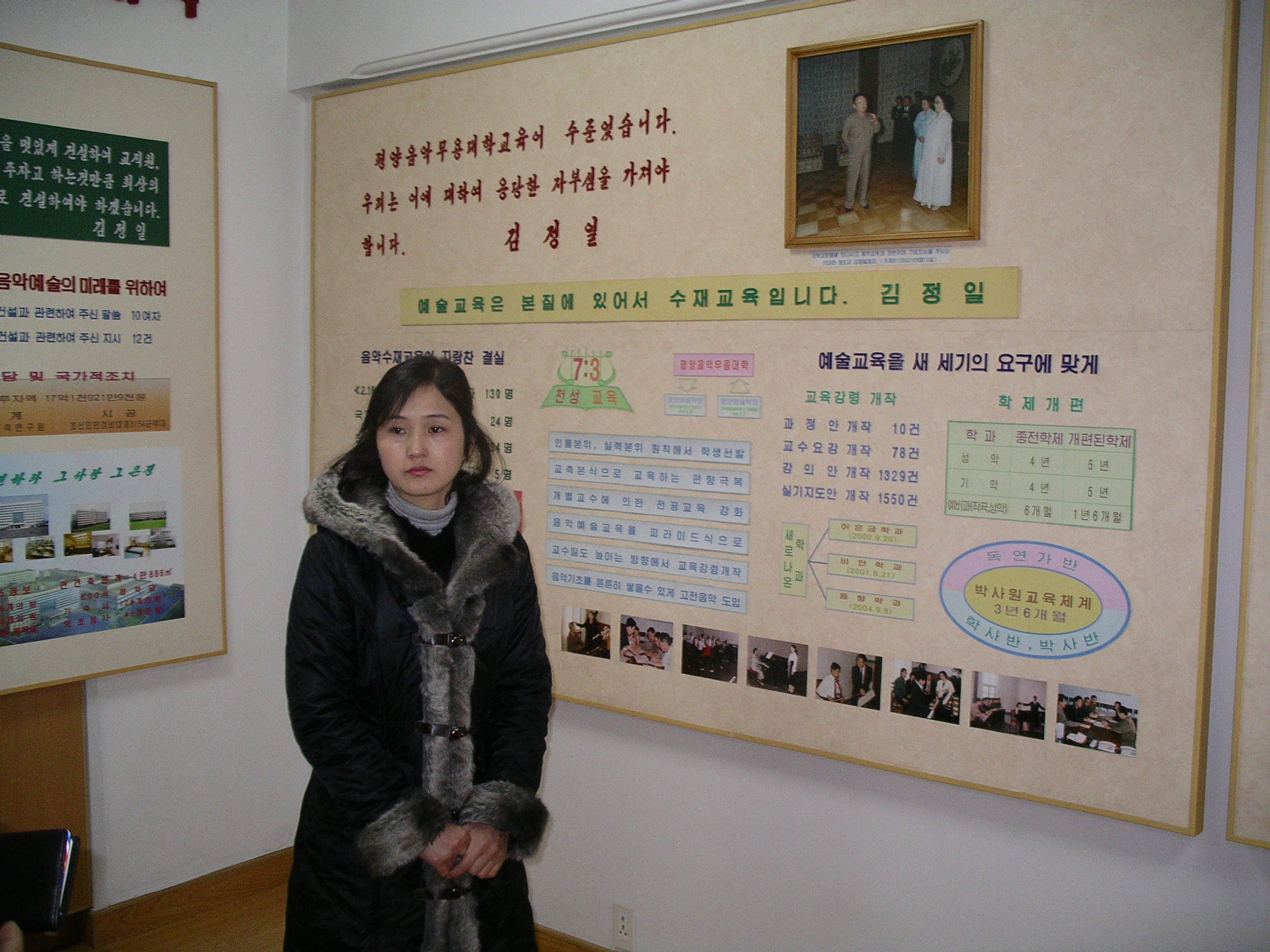 A museum guide (young woman) standing in front of a poster narrating the life of Kim Jong Il