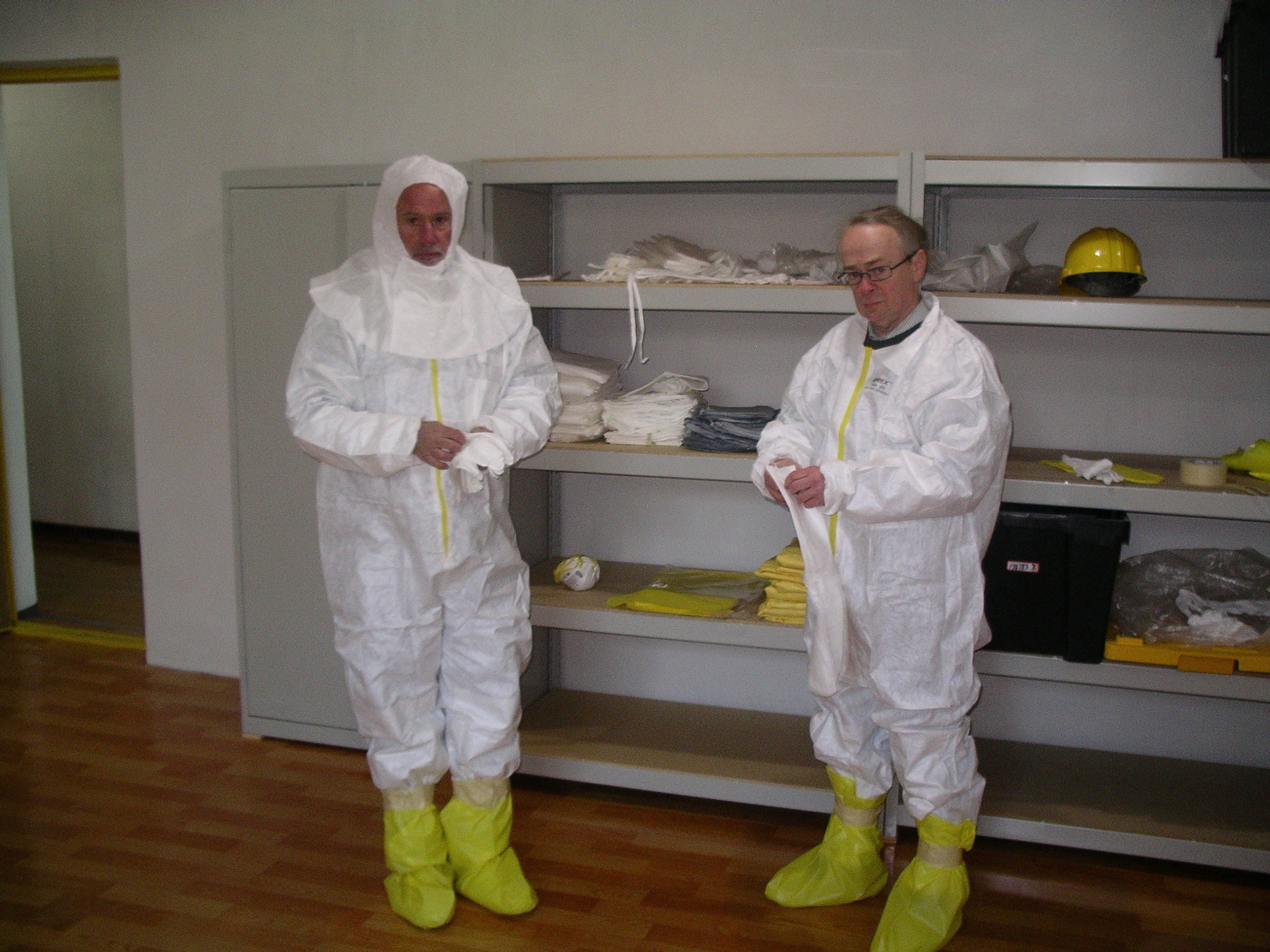 Two men donning white anti-contamination suits and wearing yellow plastic booties