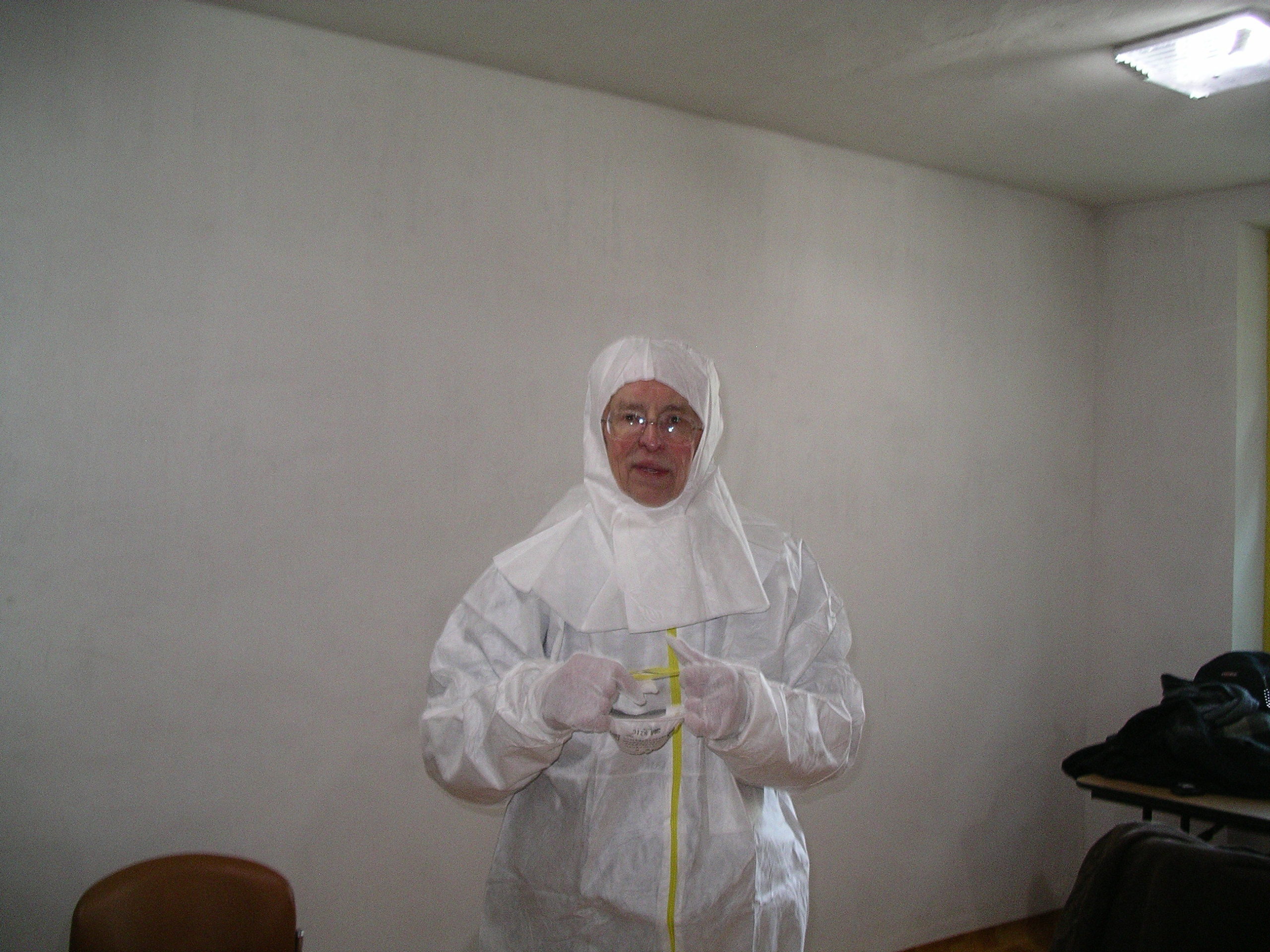 Man standing in front of a bare wall in a white anti-contamination suit