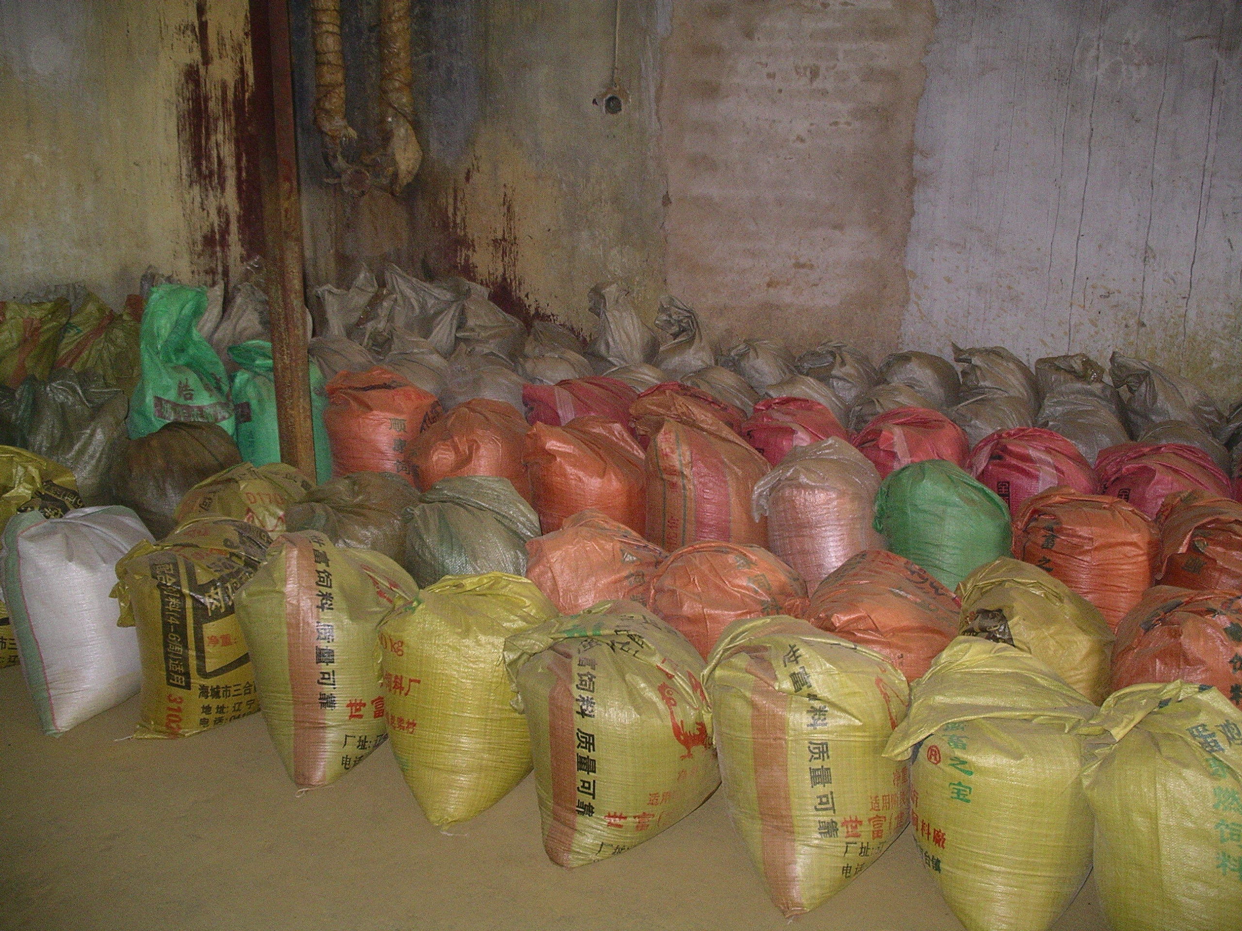 5 or more row of full plastic bags of yellow, pink, and gray color stored on a concrete floor in a large room
