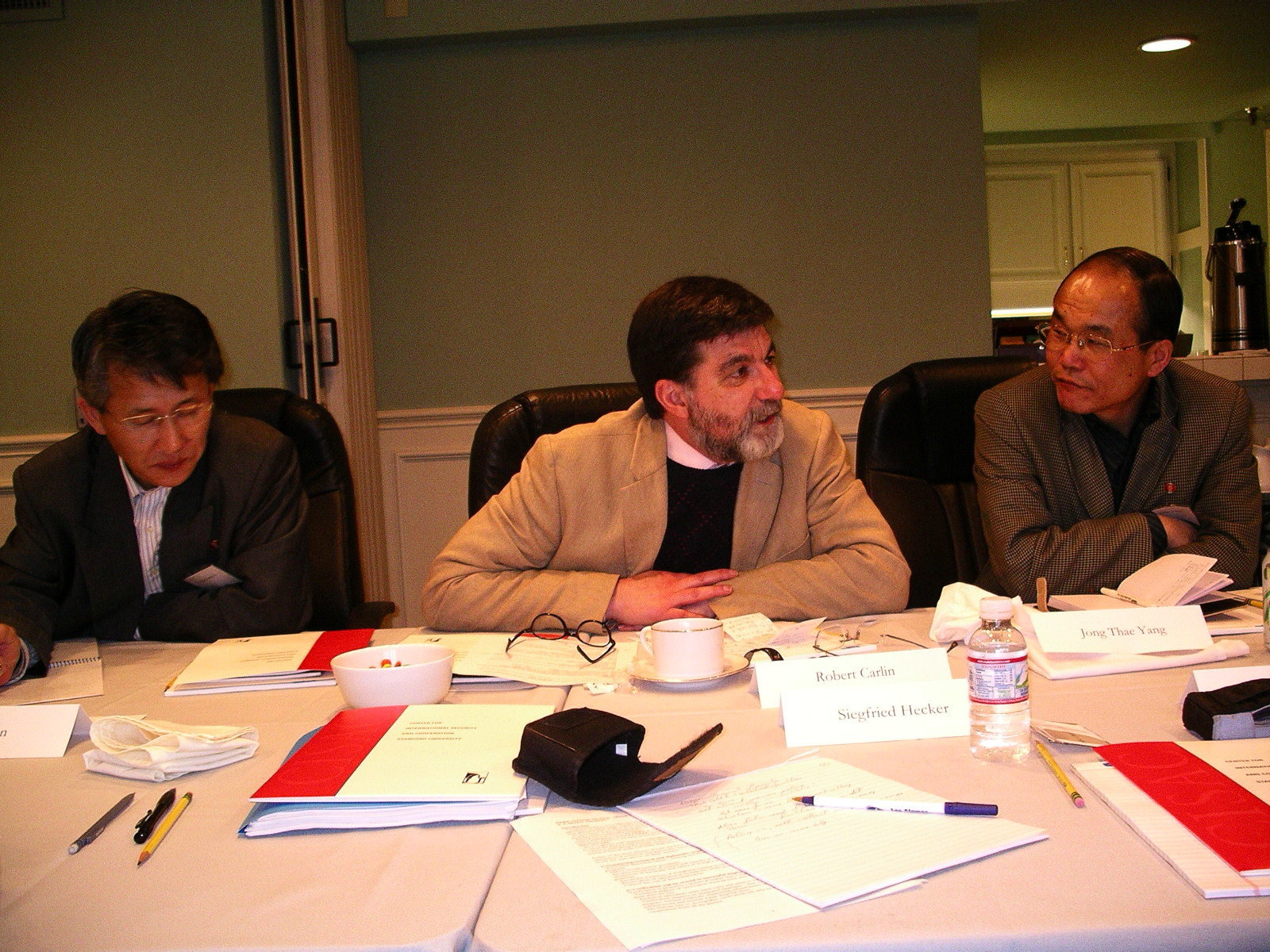 Three men at a conference table with the man in the center speaking