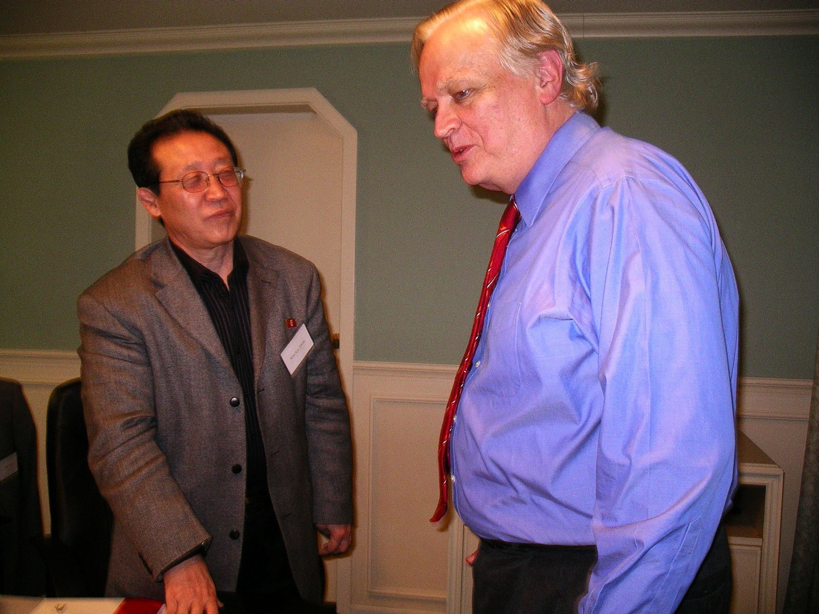 Man in blue dress shirt and tie talking to man in black shirt and jacket