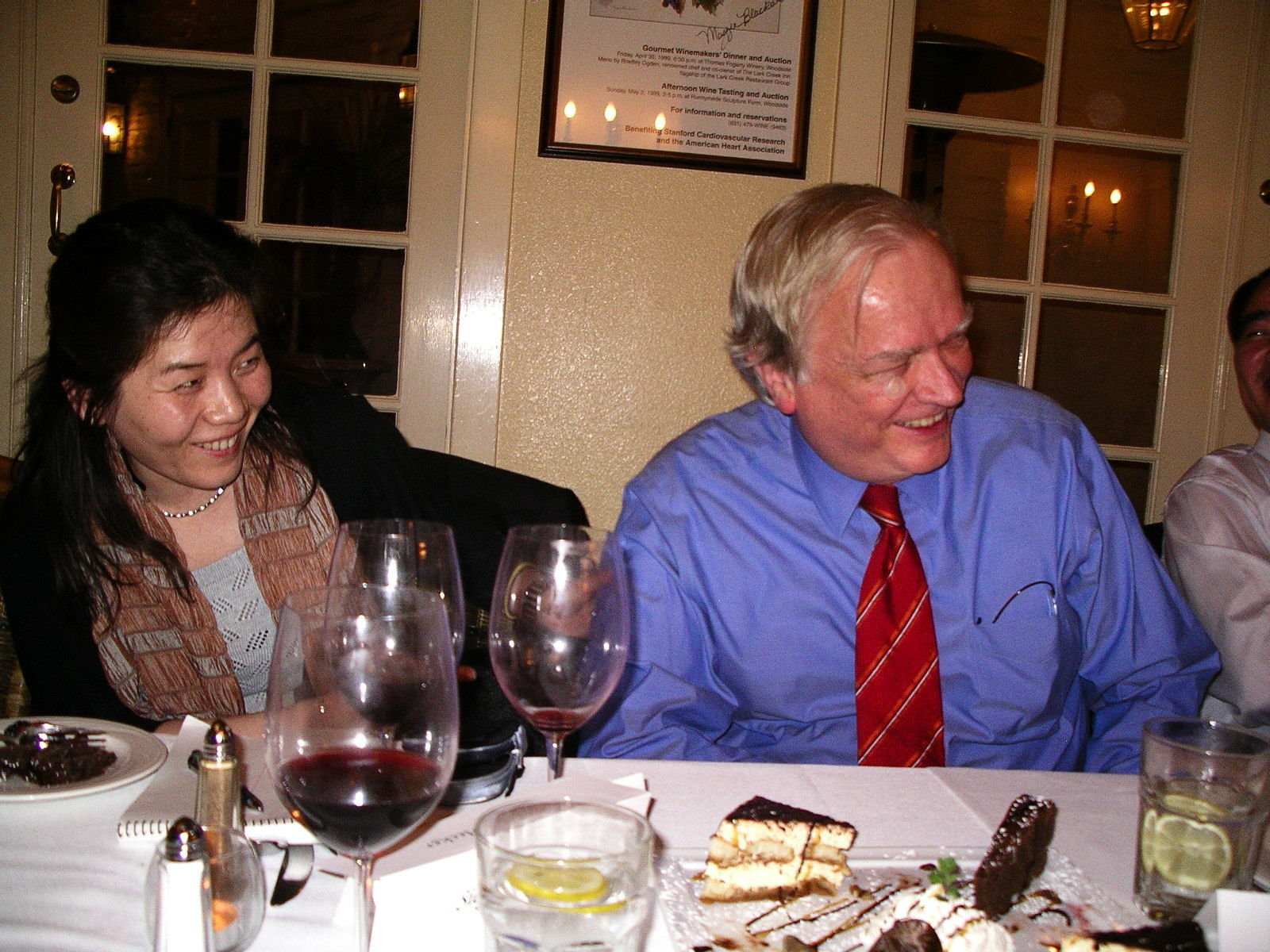 Man in blue dress shirt and woman with scarf over her neck laughing heartily sitting at the restaurant table