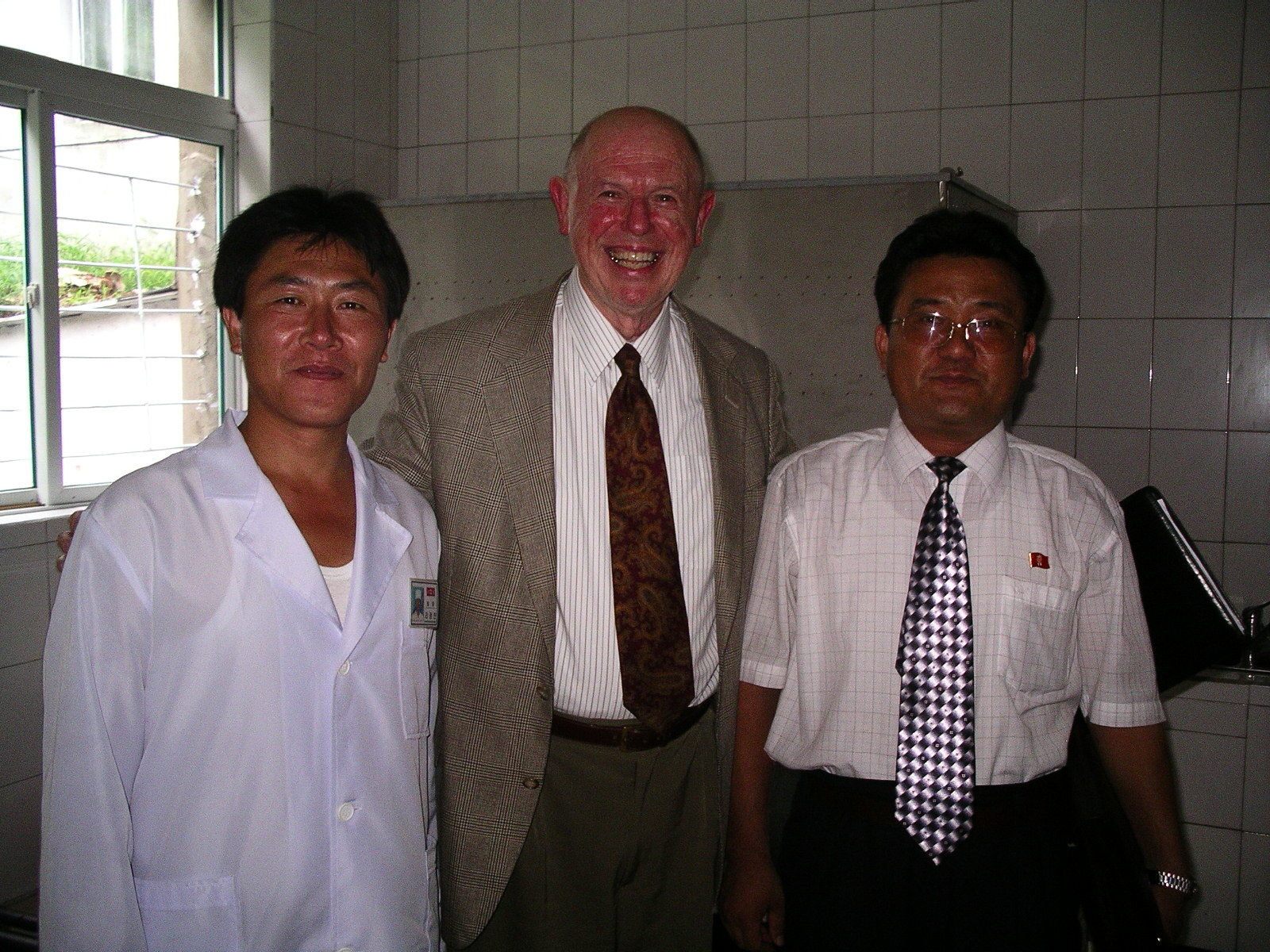 Three men posing for a photo, one of them doctor in white gown