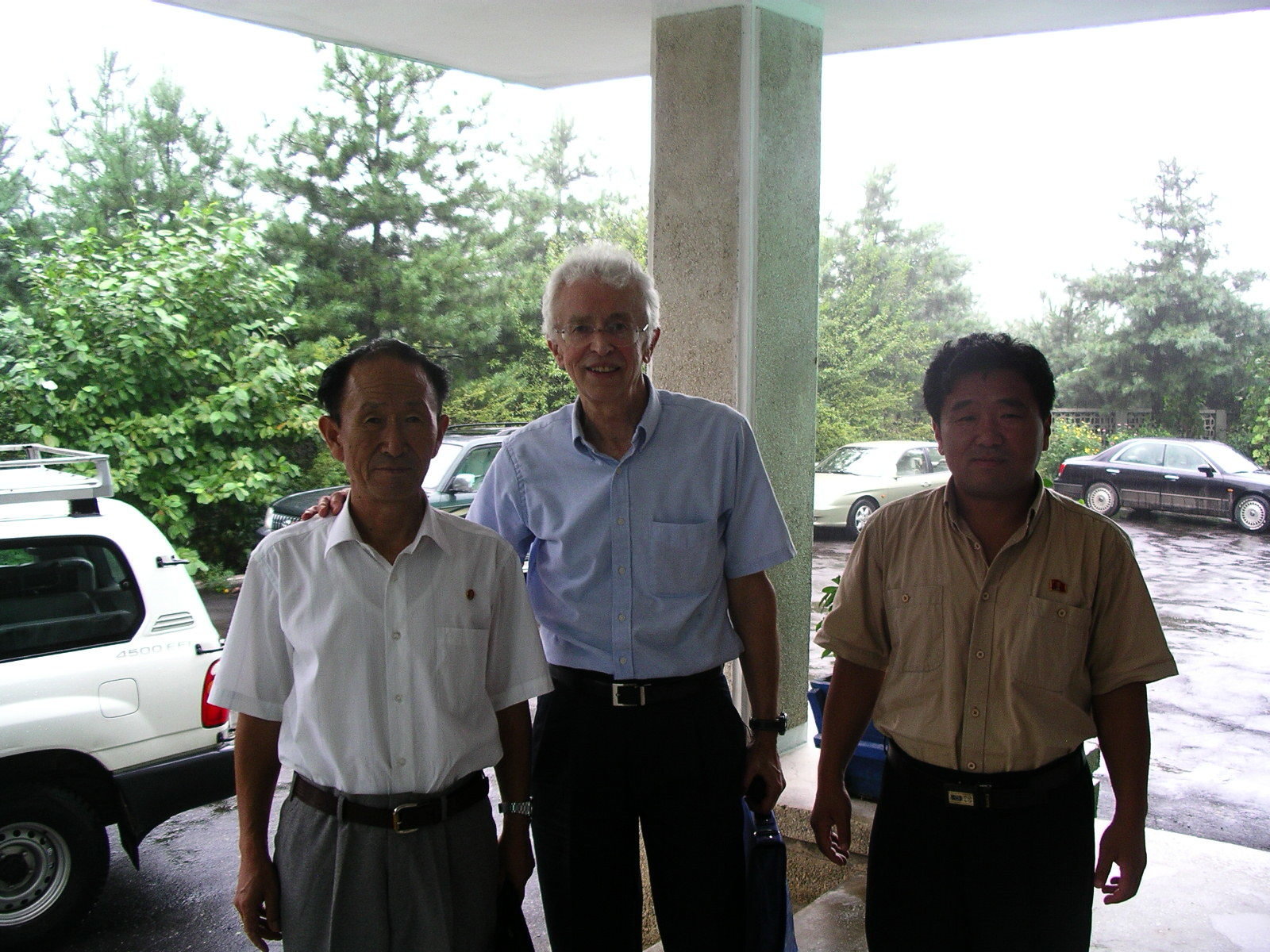 Hecker poses for photo with his hand on a shoulder of a North Korean man on his right and another North Korean man standing left.