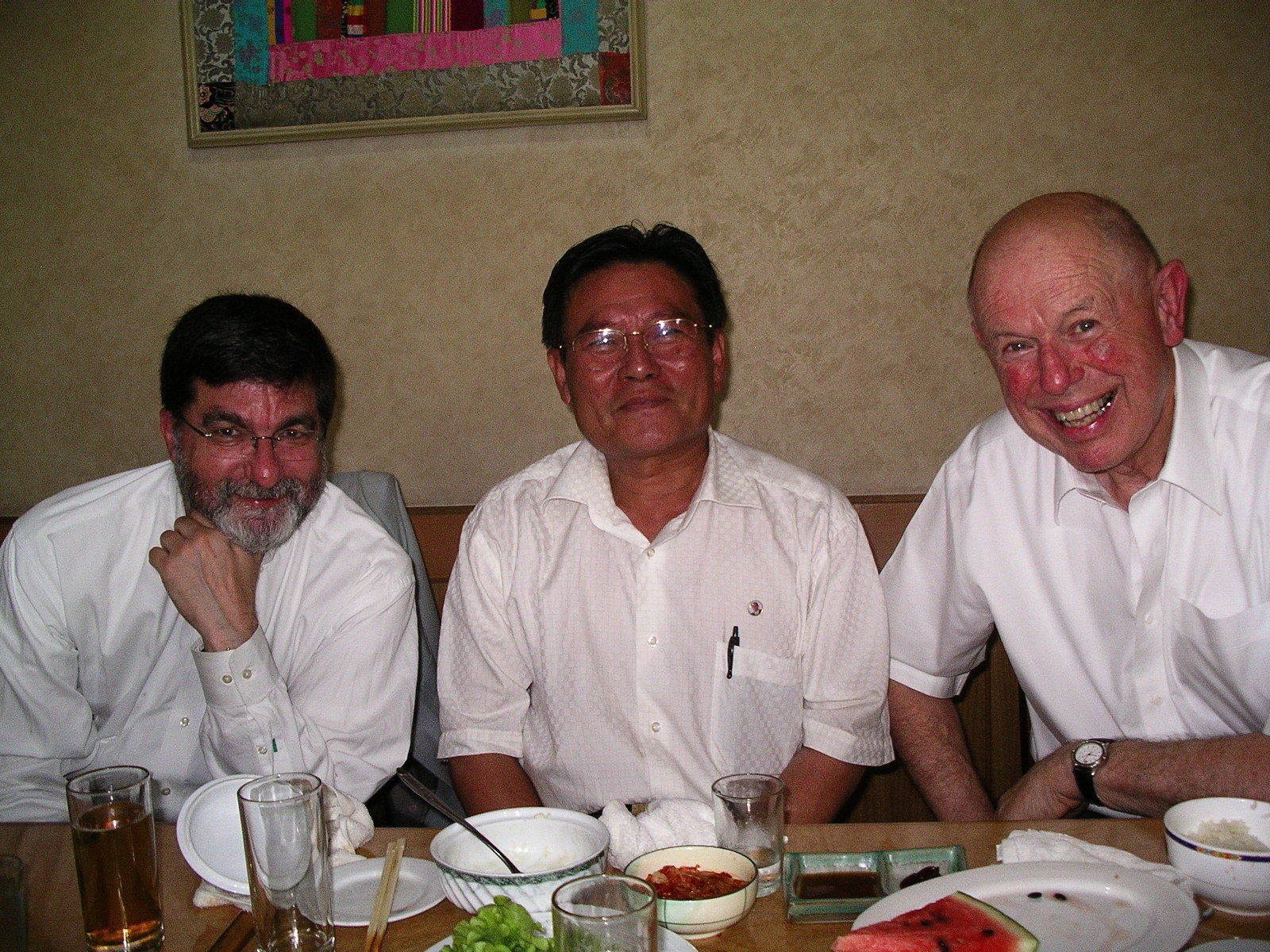Three men in light summer shirts smiling while sitting at a laid dinner table