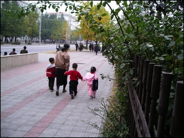 Woman walking with 3 small kids along a sidewalk in Pyongyang
