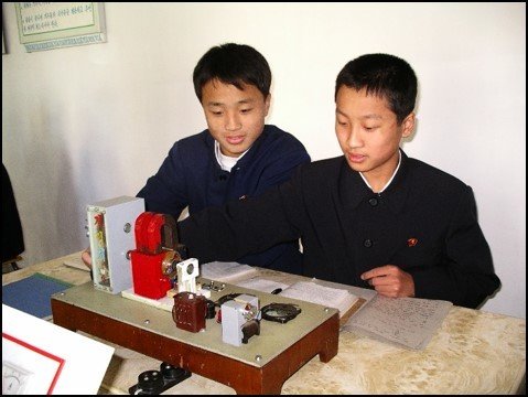 Two Korean boy students engaged with a desktop experimental installation for generating electricity