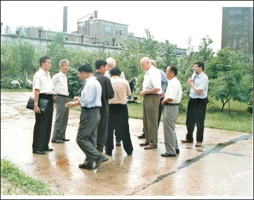Group of men in summer business attire standing on a wet concrete pad among industrial buildings