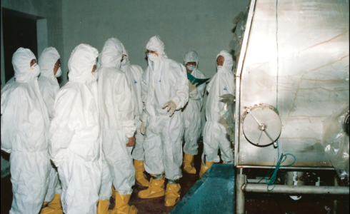 Group of people in hazmat suits and yellow booties in front of stainless steel installation for plutonium production