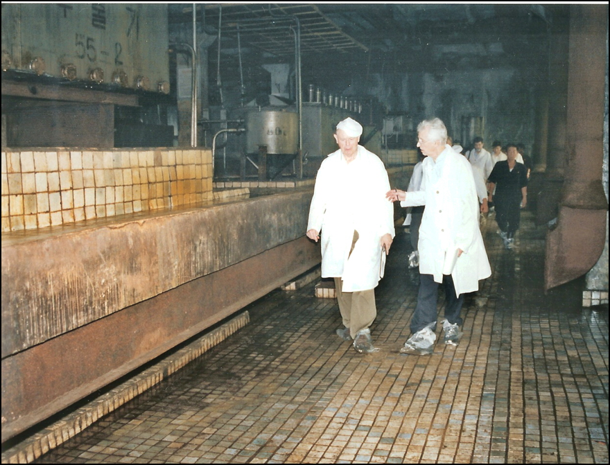 Two men in white gowns walking along an industrial dark setting