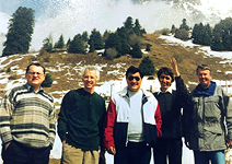 Group of men on a mountain with trees behind them and a snow spray.